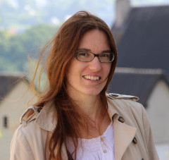 A white woman with glasses and auburn hairs, looking at the camera while smiling.